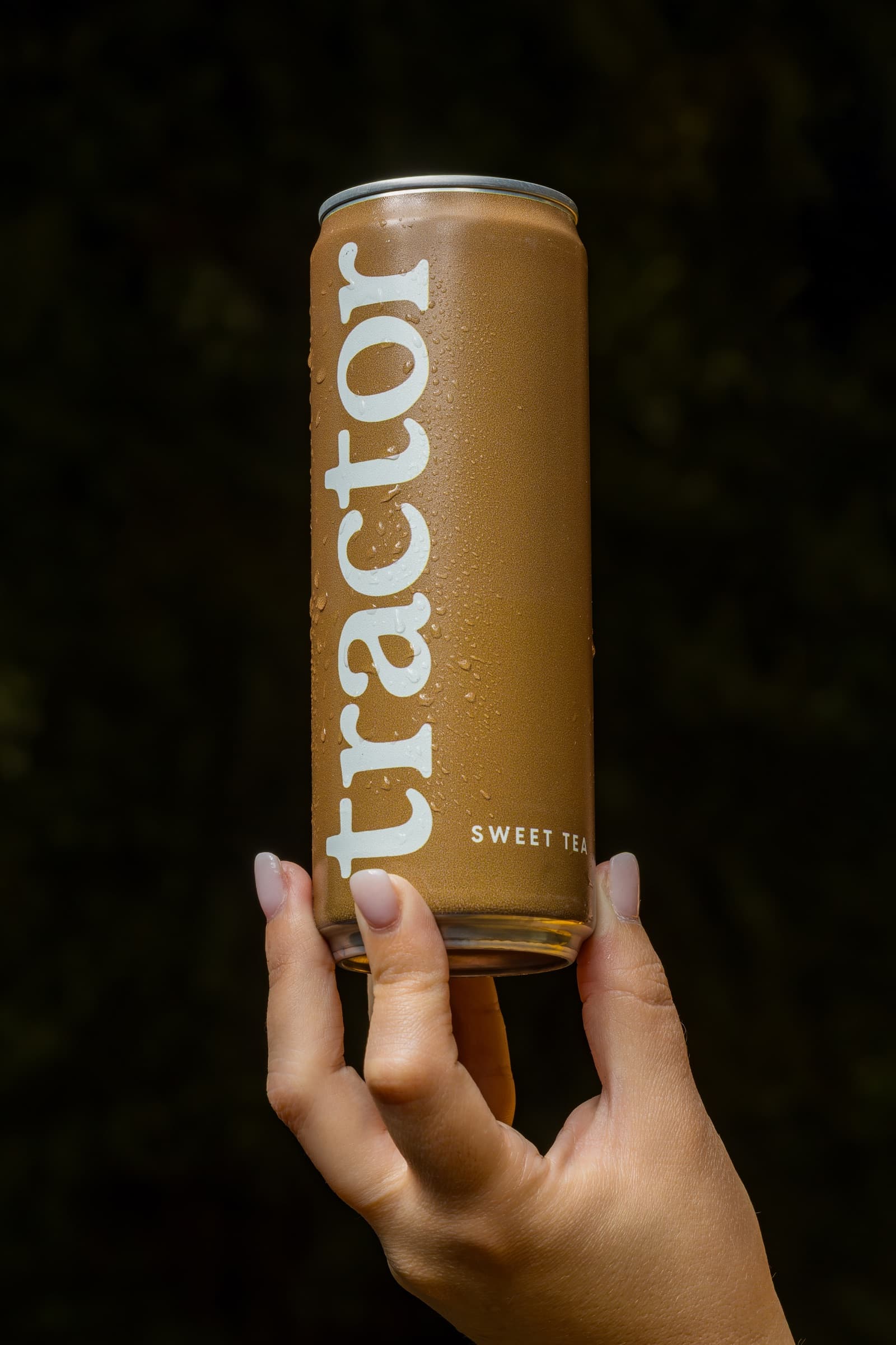 A cold can of Tráctor sweet tea held against a dark background