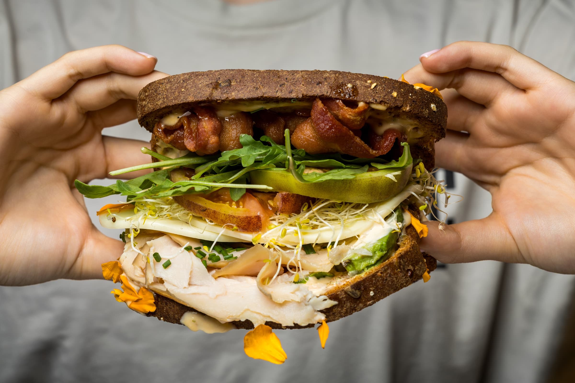 A generously stacked A Sandwich Co. sandwich held with both hands