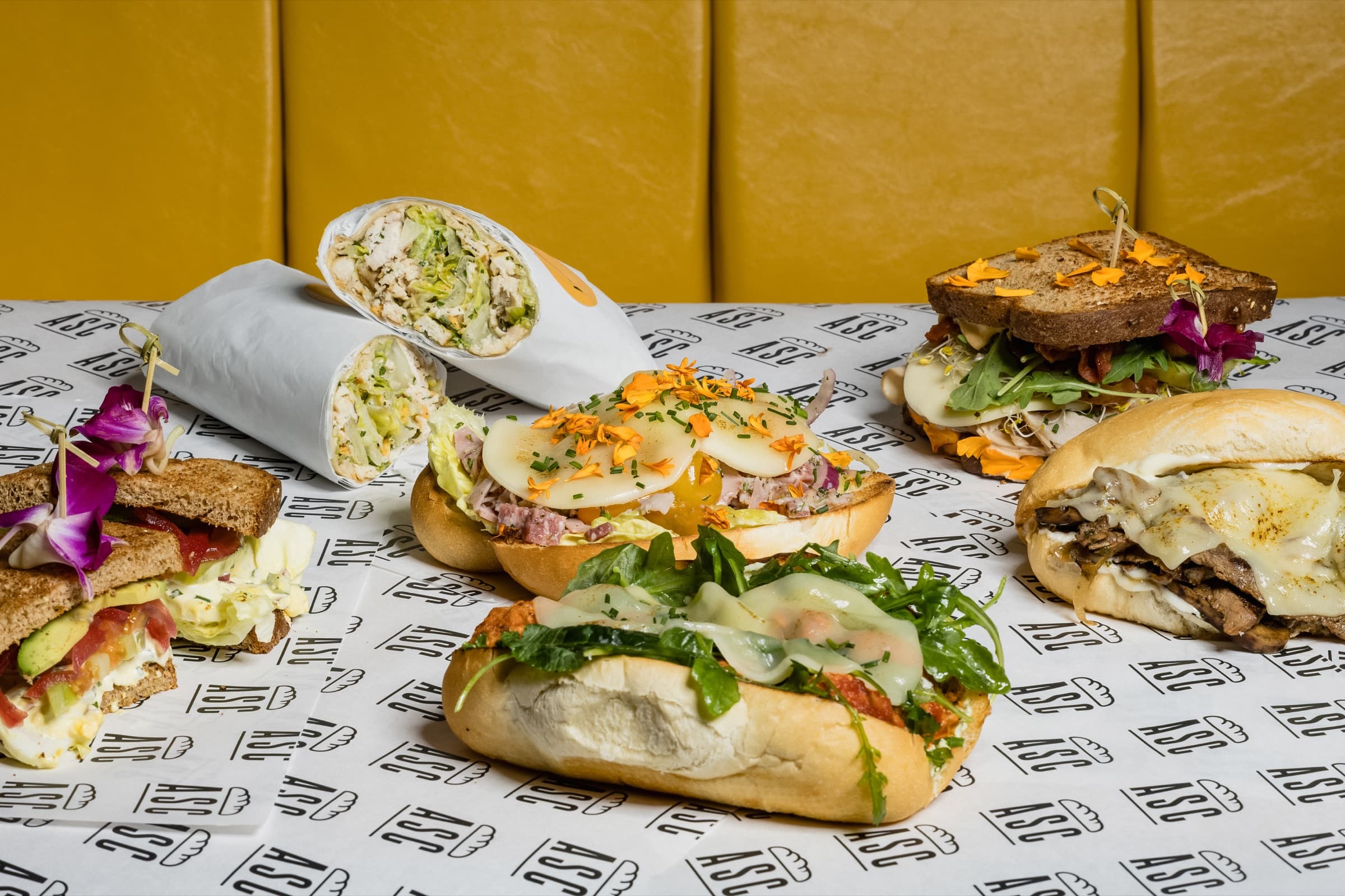 A colorful spread of A Sandwich Co. sandwiches and wraps on branded paper